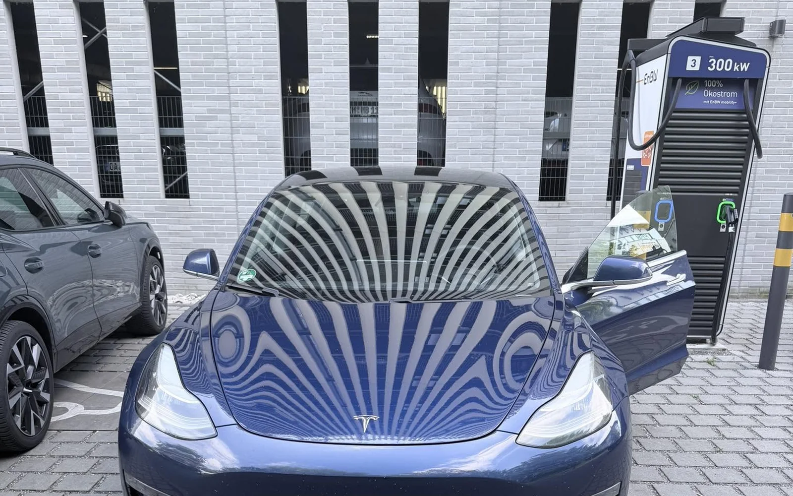 Blaues Tesla Model 3 beim Schnellladen an einer öffentlichen Ladestation