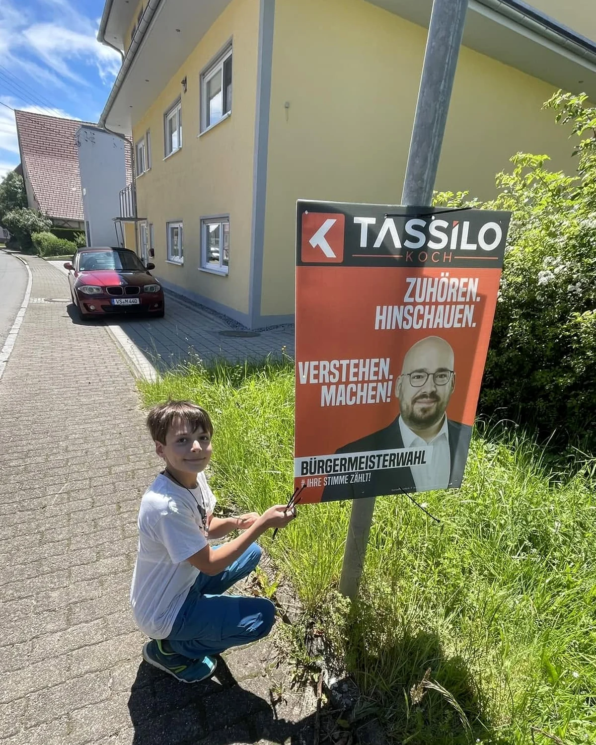 Ein junger Helfer befestigt während des Bürgermeisterwahlkampfs ein Wahlplakat am Straßenrand